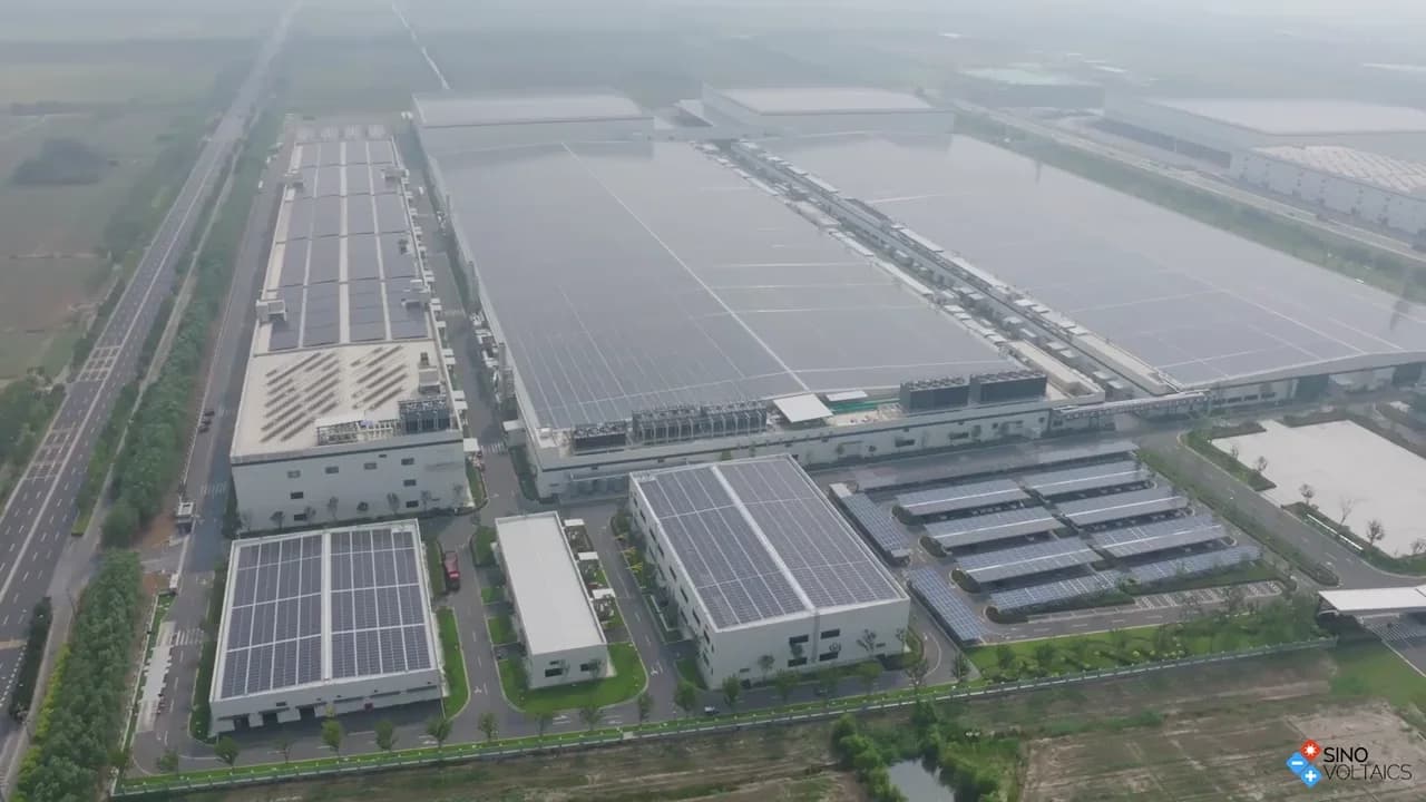 A drone view over Tongwei Solar's manufacturing campus and solar-panel-covered factory roofs, with Sinovoltaics branding.