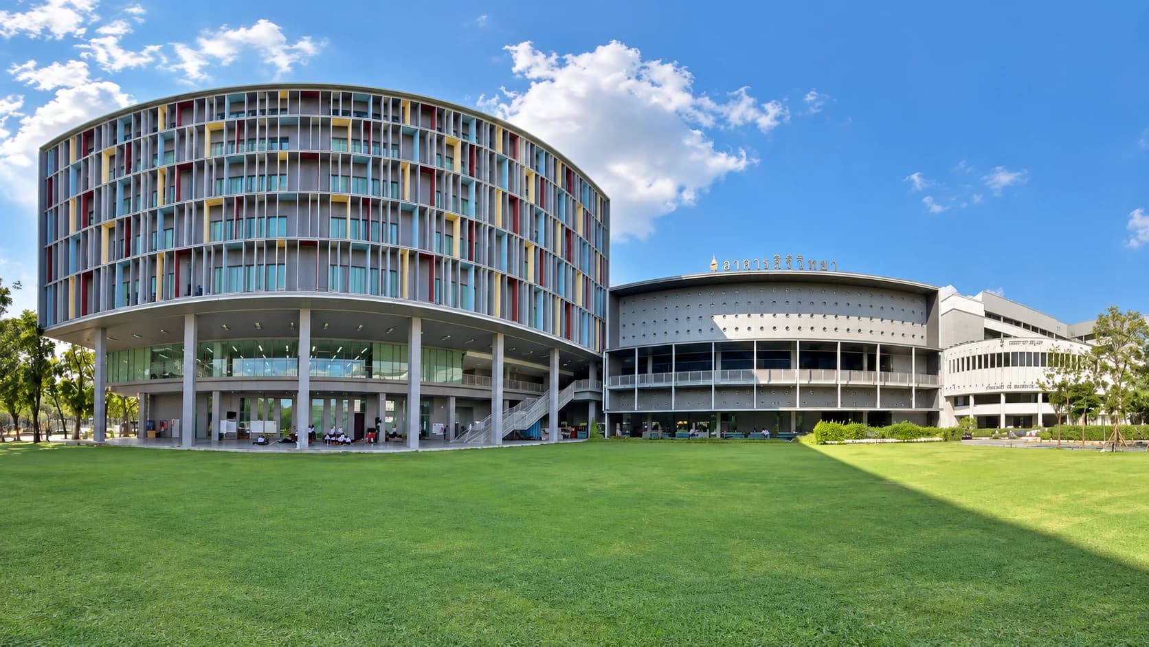 Rounded campus building with colored facade accents across a green lawn