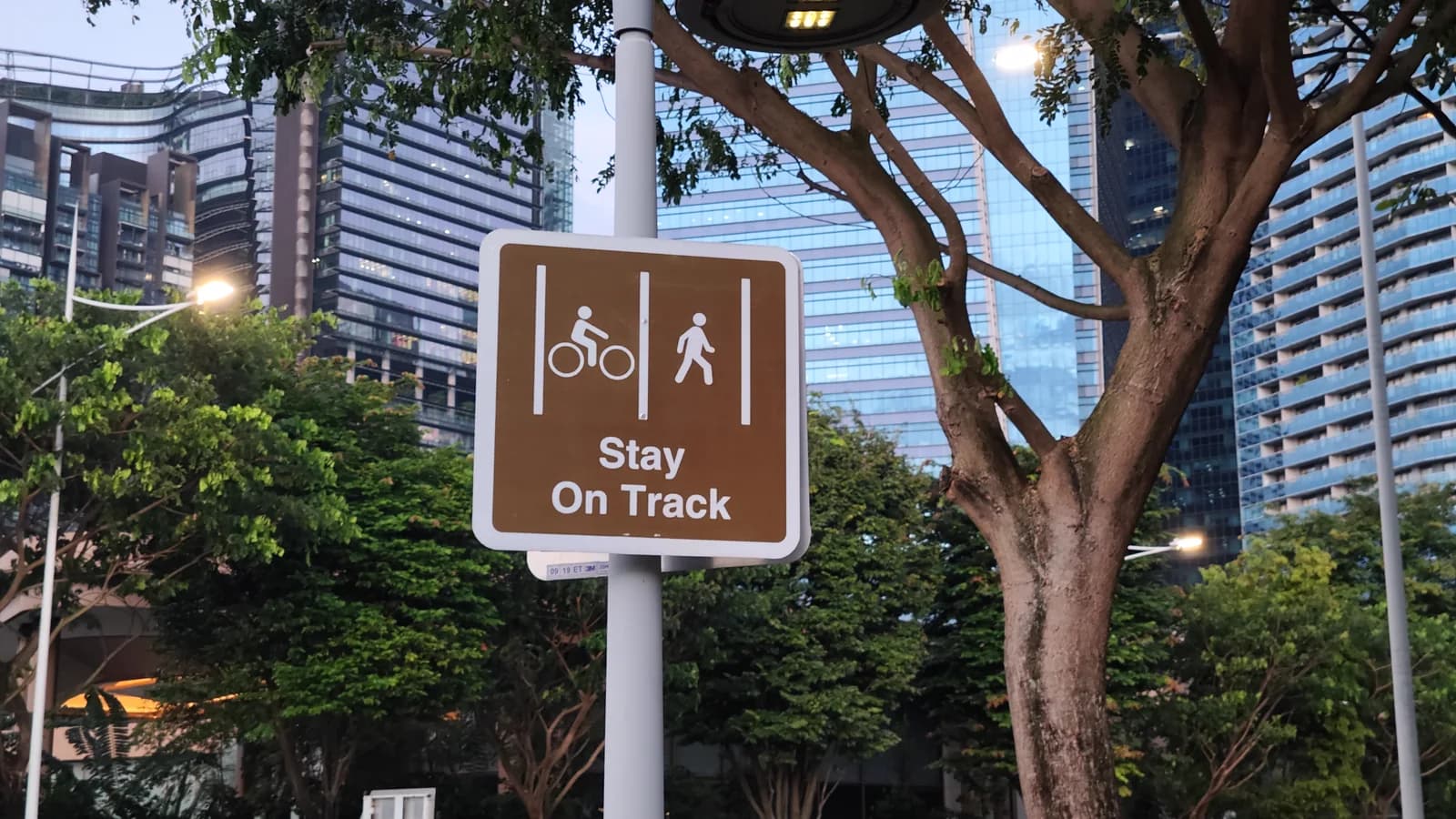 A Stay On Track sign separating cyclists and pedestrians beneath trees in Singapore